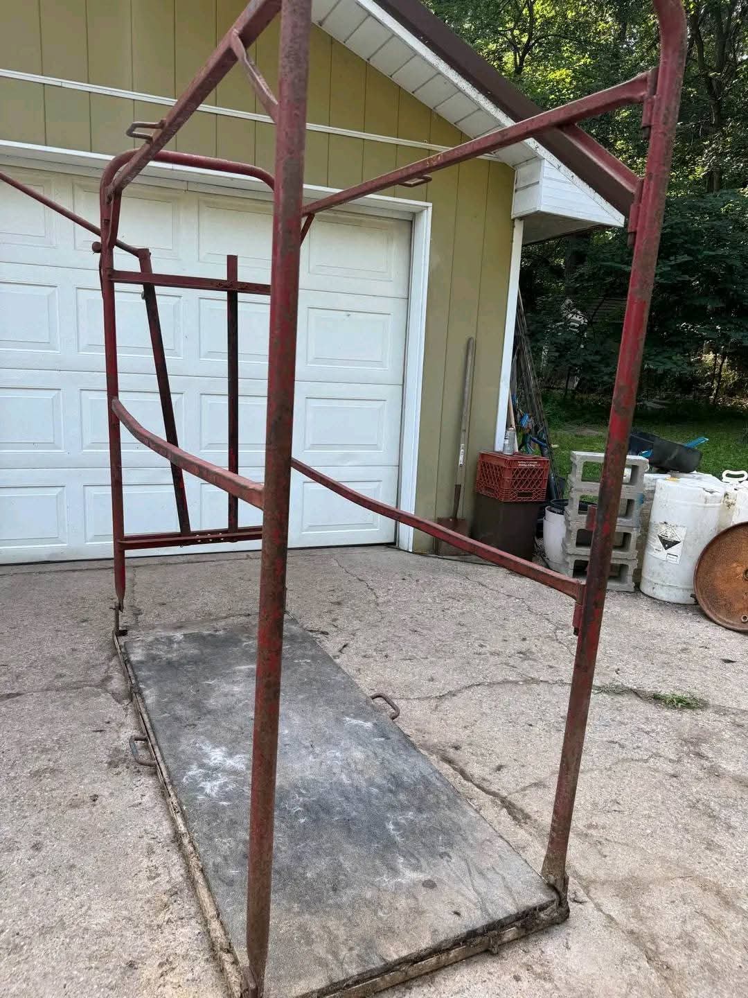 Durable steel livestock grooming chute with a red metal frame and a textured black platform base.
