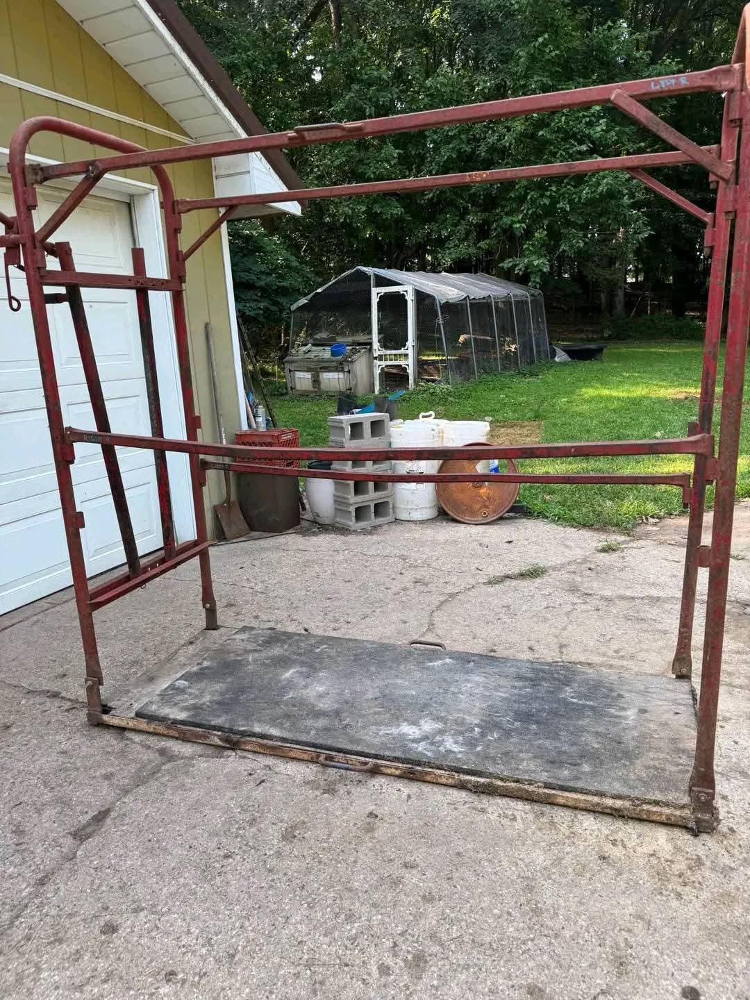 Durable steel livestock grooming chute with a red metal frame and a textured black platform base. 2