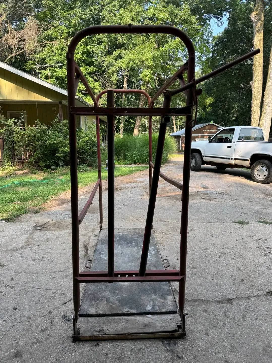 Durable steel livestock grooming chute with a red metal frame and a textured black platform base. 3